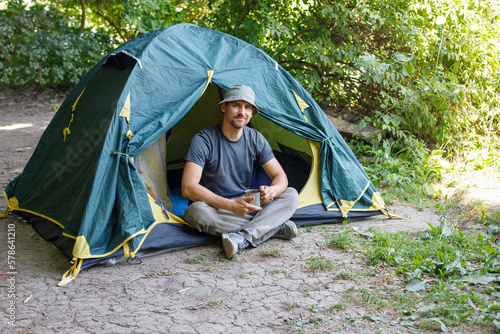 Tourist caucasian man holding cup at the tent in summer camping.