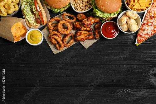 Canvastavla Burgers, onion rings and other fast food on black wooden table, flat lay with sp