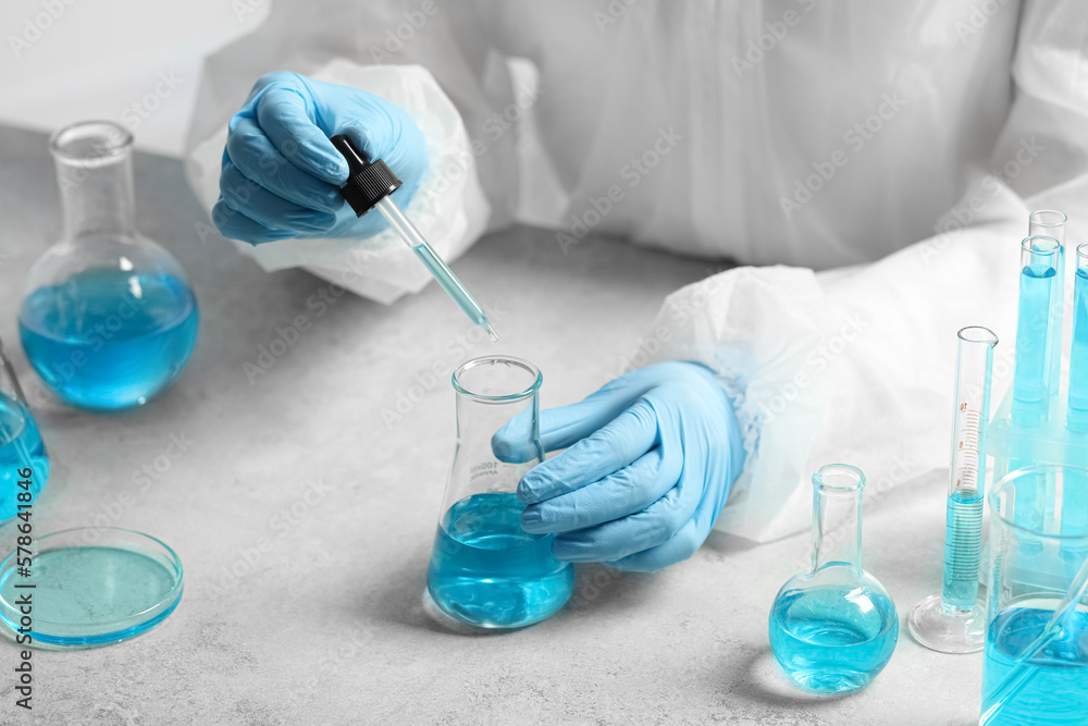 Fototapeta premium Scientist dripping liquid from pipette into beaker at white table, closeup