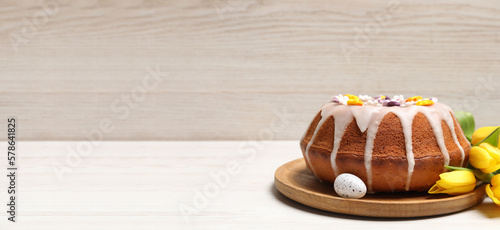 Delicious Easter cake decorated with sprinkles, egg and beautiful tulips on white wooden table, space for text. Banner design