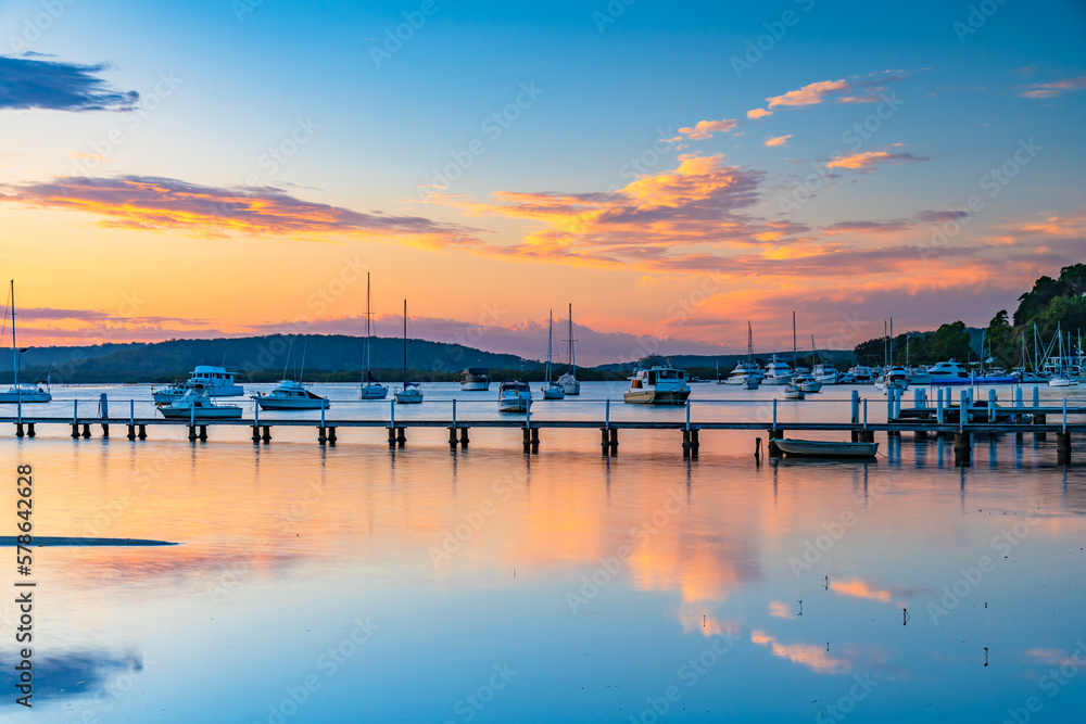 Sunrise waterscape with boats, wharf, clouds and reflections