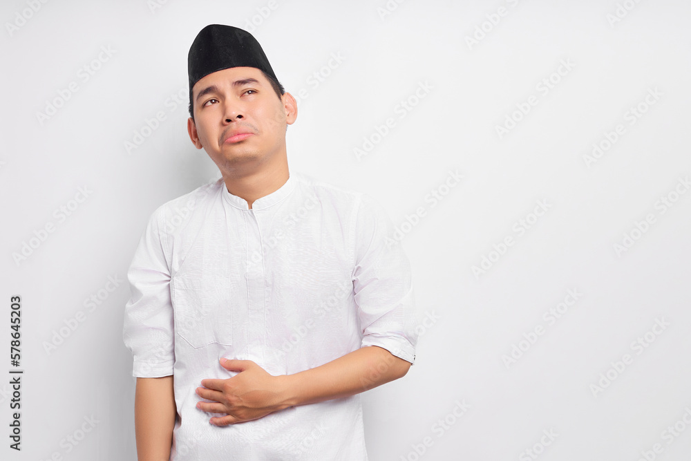 Pensive young Asian Muslim man in Arabic clothes keeping both hands on his belly, feeling hungry and wanting to eat delicious isolated on white background. People religious Islamic lifestyle concept Pensive young Asian Muslim man in Arabic clothes keeping both hands on his belly, feeling hungry and wanting to eat delicious isolated on white background. People religious Islamic lifestyle concept