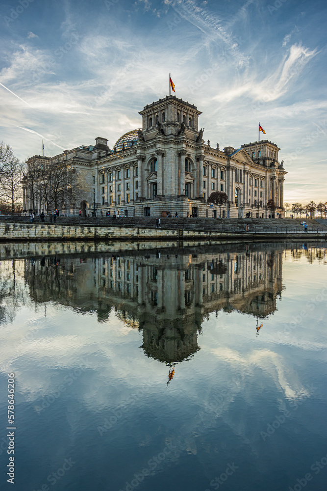 Reichstag in Berlin. German government building in the center of the capital. Spree in the foreground with reflection of the building in the sunshine. Clouds in the sky for the winter month