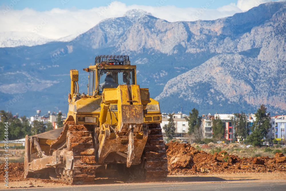 Bulldozer levels the ground in the urban area of a wasteland against the backdrop of mountains. Bulldozer levels the ground in the urban area of a wasteland against the backdrop of mountains.