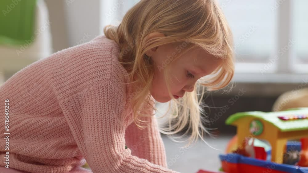 Cute little blond girl plays on the floor busily being alone, autistic child avoids team activities. Thoughtful kid, bright nursury background, natural daylight. Mental health diseases. HQ 4k footage Cute little blond girl plays on the floor busily being alone, autistic child avoids team activities. Thoughtful kid, bright nursury background, natural daylight. Mental health diseases. HQ 4k footage