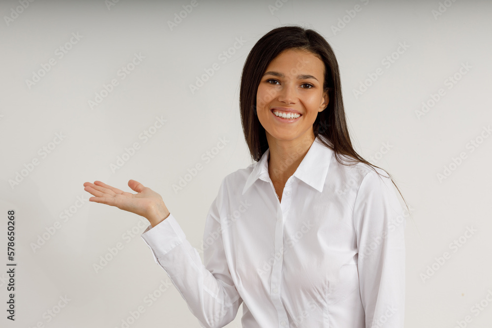 Portrait of happy smiling brunette girl dressed in white shirttemplate empty holding hand palm. Beautiful model on isolated white background. Studio shot of young attractive woman in business Portrait of happy smiling brunette girl dressed in white shirttemplate empty holding hand palm. Beautiful model on isolated white background. Studio shot of young attractive woman in business