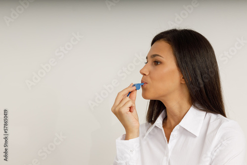 Portrait of attractive smiling girl brunette holding blue whistle in her hand and looking at the camera. Happy young woman with long hair in white shirt on isolated background. Fan, coach, counselor.