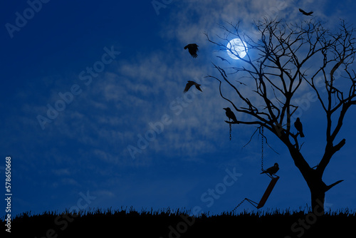 Silhouette of a dry tree outdoors with an old swing broken chain and surrounding crow birds at full moon night.