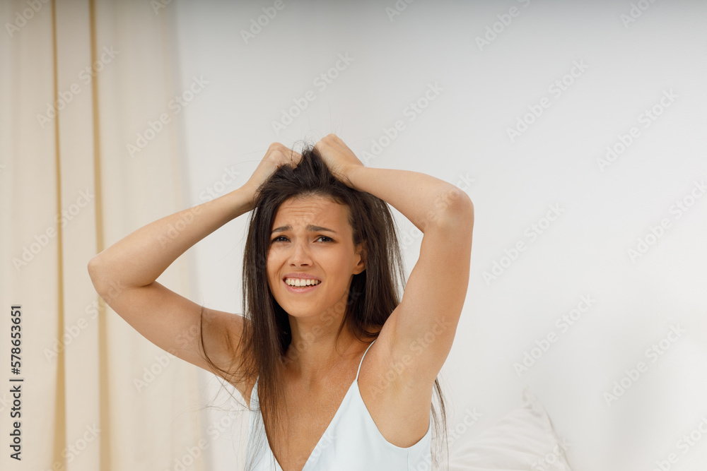 Attractive girl headache, it's time to get up for work. Beautiful young woman, dressed in silk negligee of delicate blue color, is sitting in cozy bed in the bedroom, holding her head. Attractive girl headache, it's time to get up for work. Beautiful young woman, dressed in silk negligee of delicate blue color, is sitting in cozy bed in the bedroom, holding her head.