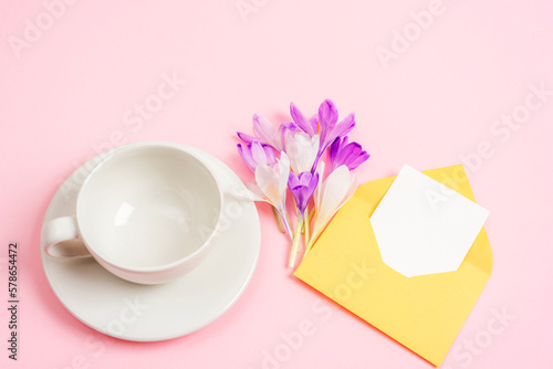 Empty coffee cup, bouquet of spring flowers and envelope with blank card. Top view, mockup