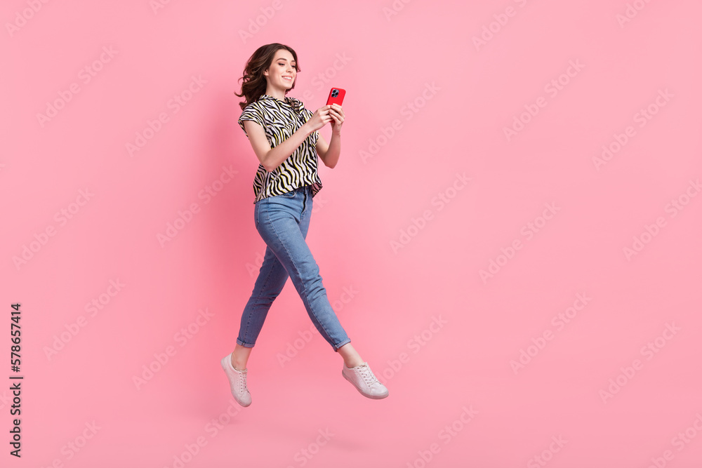 Full length photo of cheerful pretty person jumping use smart phone empty space ad isolated on pink color background Full length photo of cheerful pretty person jumping use smart phone empty space ad isolated on pink color background