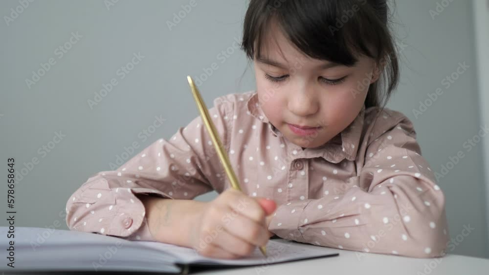 Little girl is writing the essay in notebook at home. Online learning, homeschooling. Kid is doing homework concept. Selective focus Little girl is writing the essay in notebook at home. Online learning, homeschooling. Kid is doing homework concept. Selective focus