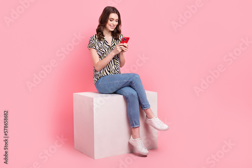 Full body portrait of nice cheerful lady sit podium use telephone typing post isolated on pink color background