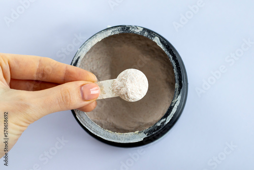Black jar with electrolytes in measuring spoon in woman's hand on white background, top view