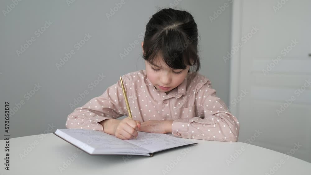 Little girl is writing the essay in notebook at home. Online learning, homeschooling. Kid is doing homework concept. Selective focus Little girl is writing the essay in notebook at home. Online learning, homeschooling. Kid is doing homework concept. Selective focus