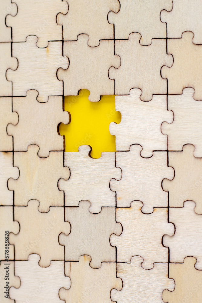 Assembled puzzle background. One missing wooden puzzle on a yellow background. The concept of completing a case. Vertical Photo. Assembled puzzle background. One missing wooden puzzle on a yellow background. The concept of completing a case. Vertical Photo.