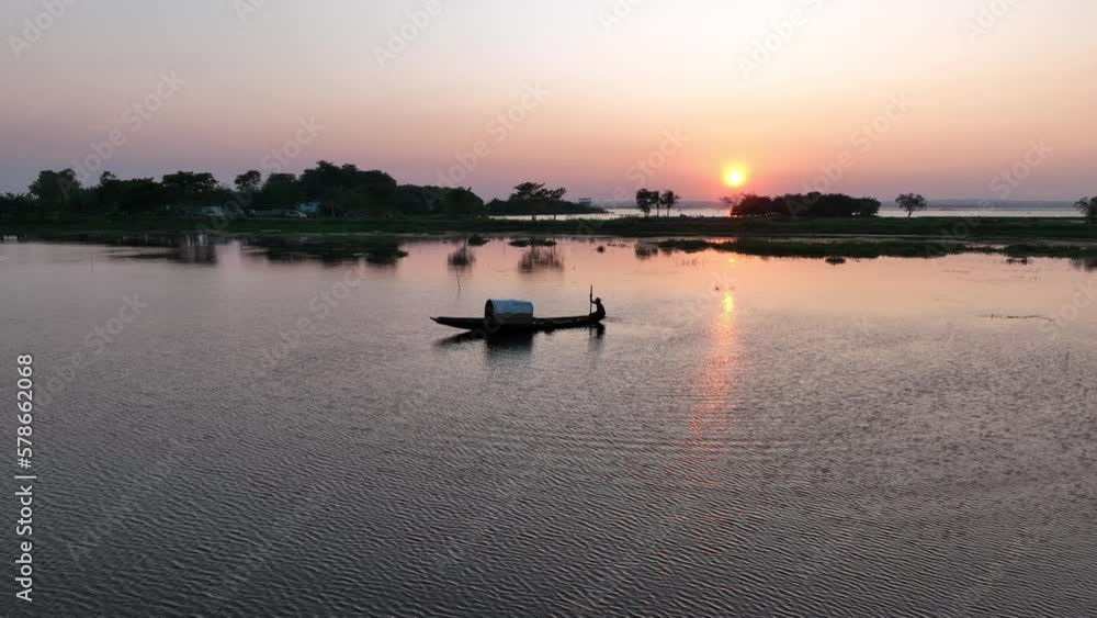 Traditional boat moving slowly along the lake with the sunset in the background. Bangladesh. Traditional boat moving slowly along the lake with the sunset in the background. Bangladesh.