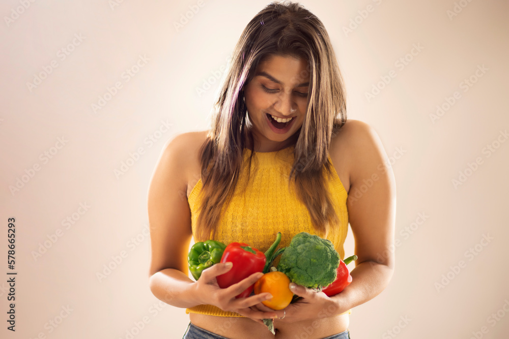 Smiling woman holding a basket of fresh vegetables against white background Smiling woman holding a basket of fresh vegetables against white background