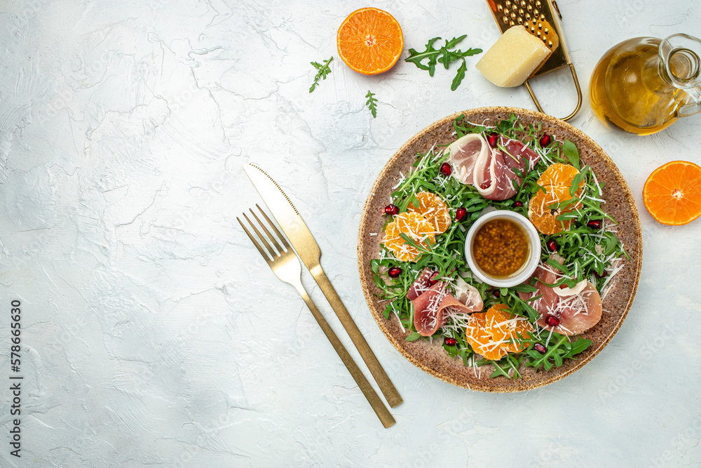 Delicious salad with arugula mandarins, prosciutto jamon and Parmesan cheese on blue background. Long banner format. top view