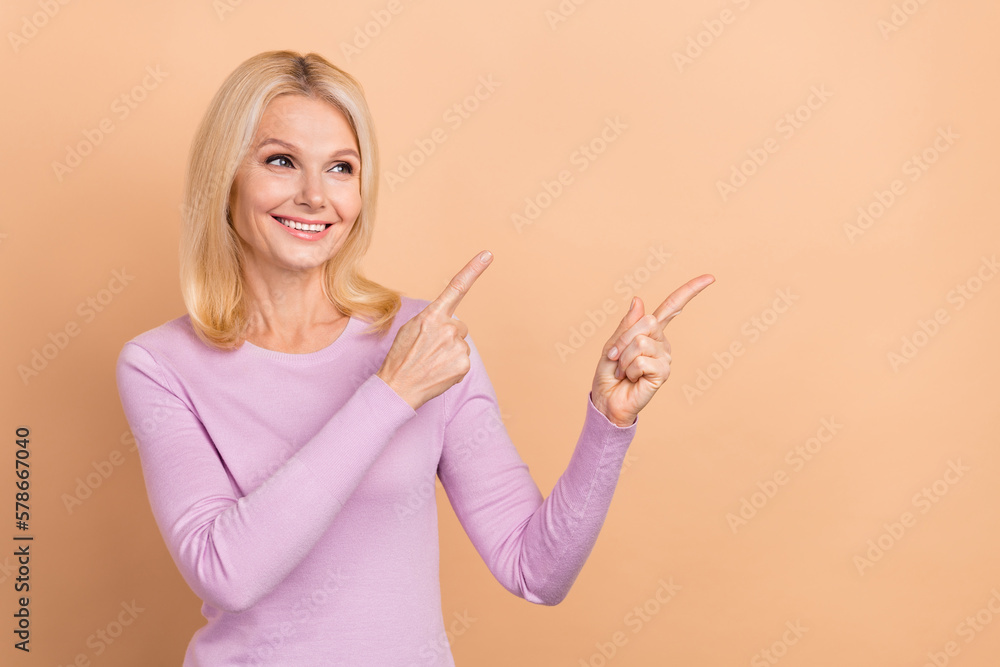 Photo of mature lady wear violet shirt pointing fingers look copyspace useful tips get free delivery promo code isolated on beige color background Photo of mature lady wear violet shirt pointing fingers look copyspace useful tips get free delivery promo code isolated on beige color background