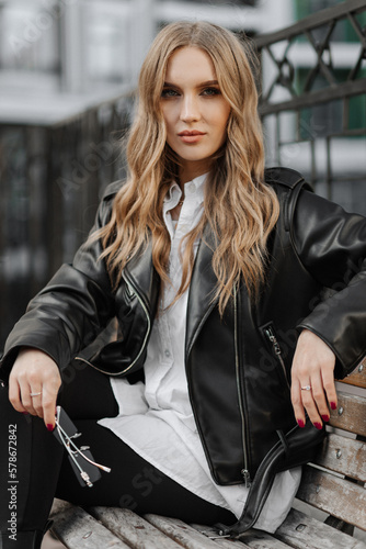 Close up portrait of a beautiful smiling young blonde woman in a black leather jacket on the  a city street background