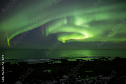 Bright winding aurora borealis over rocky beach waves Iceland