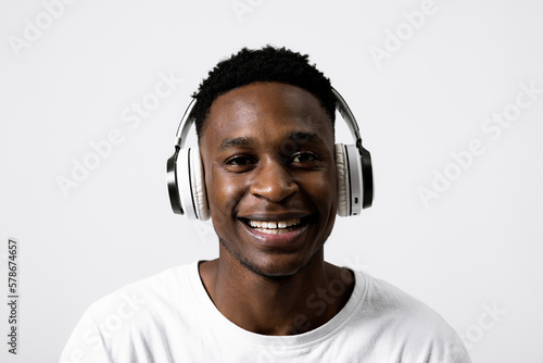 Close up shot selective focus on portrait of delighted handsome african american man wearing modern new white headphones earphones listening to music having fun standing over white background studio.