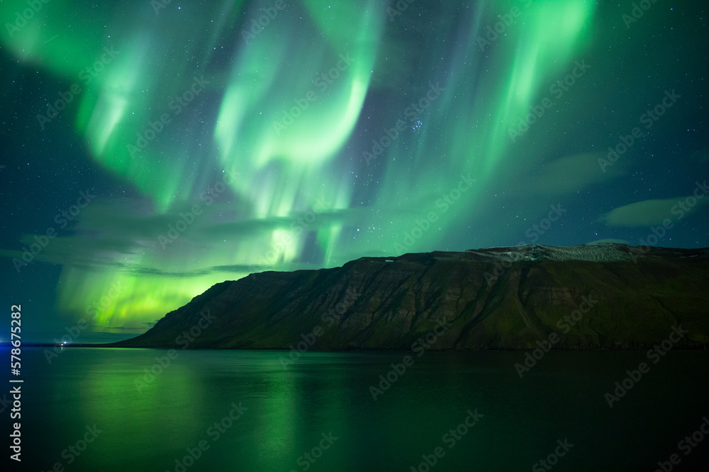 Extremely bright aurora borealis reflecting in ocean fjord Iceland