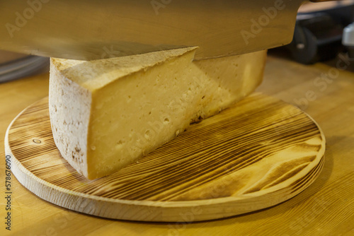 A man cuts a head of cheese with a large knife.