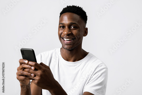 Happy delighted african american black man holding new modern last series smartphone in hands advertisement concept smiling messaging receiving goor news chatting with friends. © ABCreative