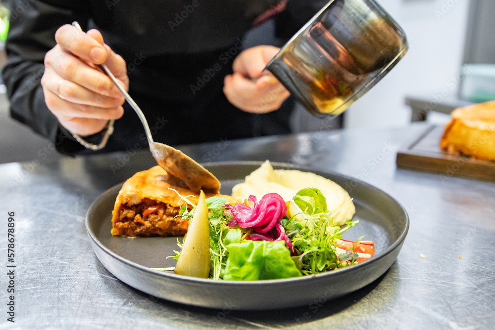 chef hand preparing Meat Pie with mashed potato and salad on restaurant kitchen
