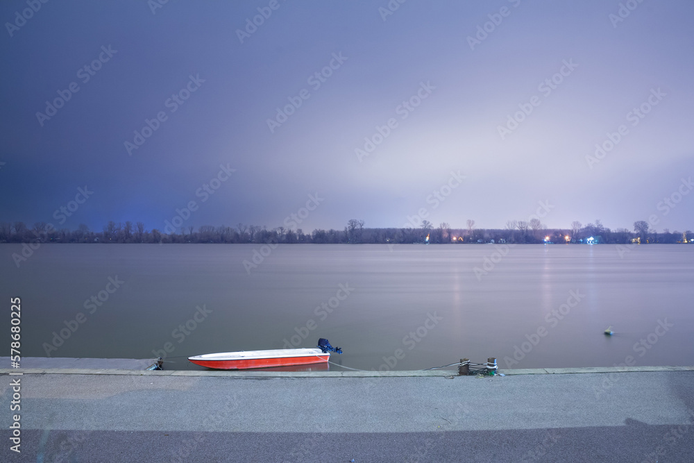 Obraz premium Selective blur on a log exposure of a Small boat, fisherman ship; anchored standing on the riverbanks of the river Dabube on Zemunski Kej, in Zemun, a suburb of Belgrade, Serbia, at night in winter.