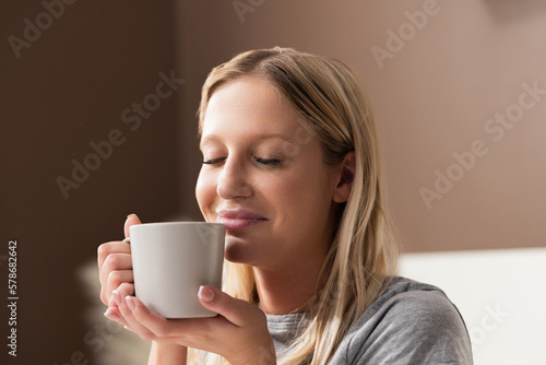 Young beautiful blond lady woman in gray pajama holding cup of coffee in hands sniffing tired ill sick lady on quarantine relaxing resting on holidays at gome isolated.