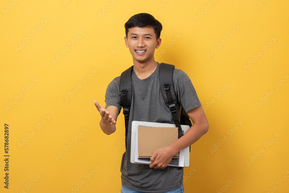 Smiling young college student with books and backpack isolated on yellow background friendly offering handshake to get acquainted