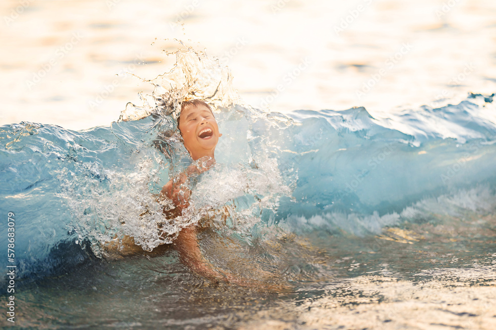 Happy child plays with sea waves. Child splashes in water on shore. Kids summer vacation.