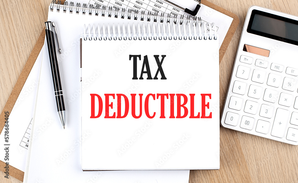 TAX DEDUCTIBLE is written in white notepad near a calculator, clipboard and pen. Business concept TAX DEDUCTIBLE is written in white notepad near a calculator, clipboard and pen. Business concept