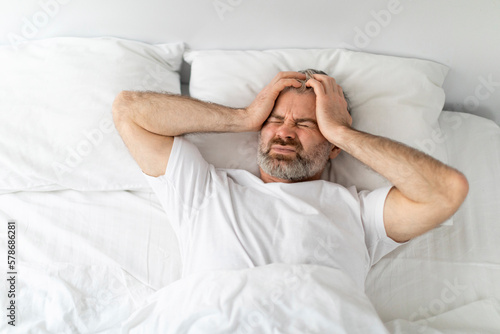 Unhappy middle aged man lying in bed  touching head