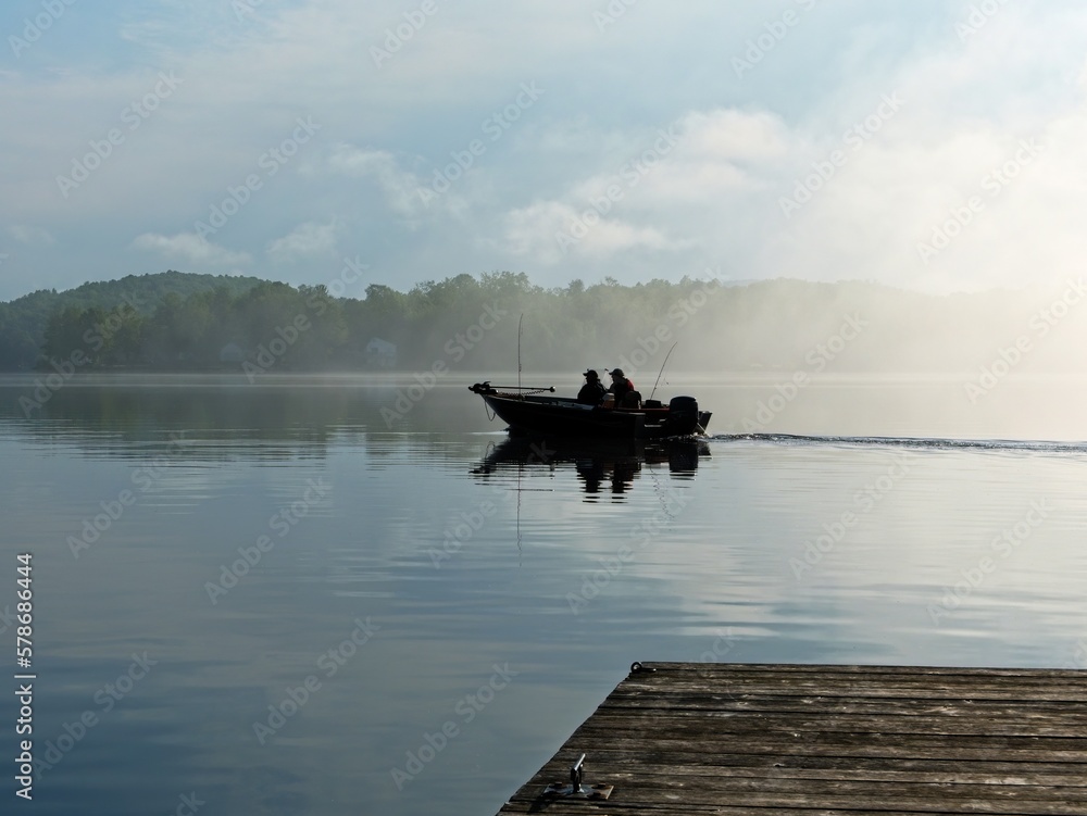 Silhouette of two fishermen in a small boat on a calm lake in the fog early in the morning