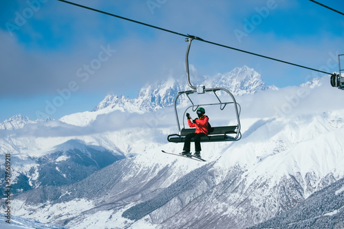 Skier sitting on Chair ski lift at ski resort against backdrop of amazing mountain peaks covered with snow