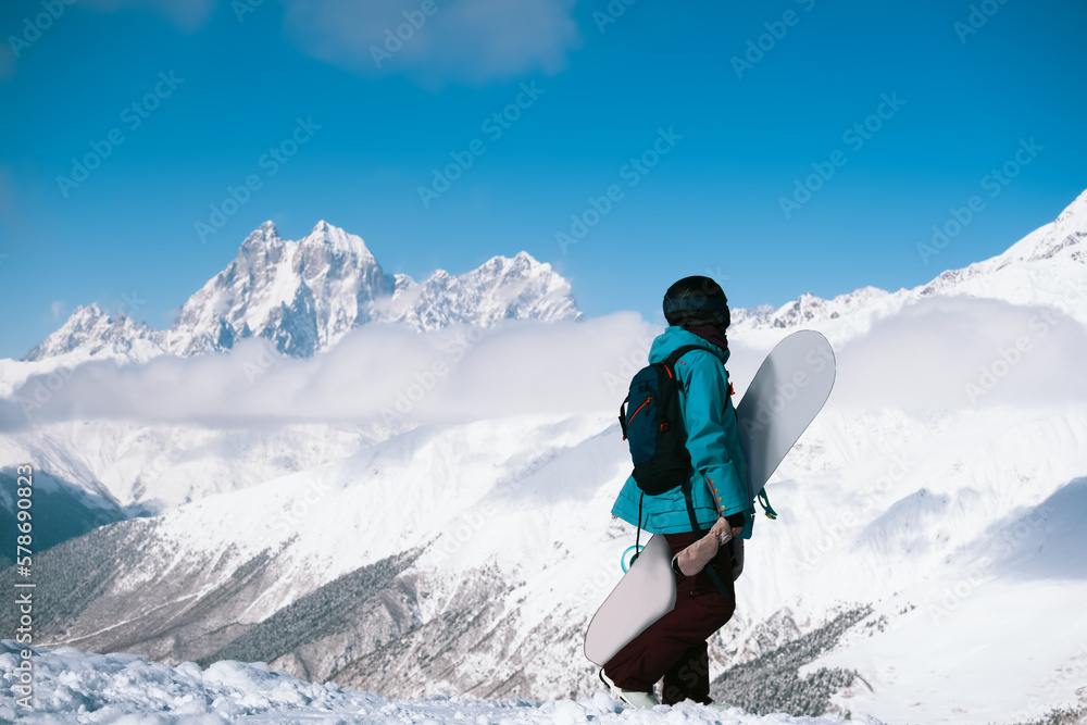 Snowboarder woman standing with snowboard beautiful mountain peaks covered with snow on background