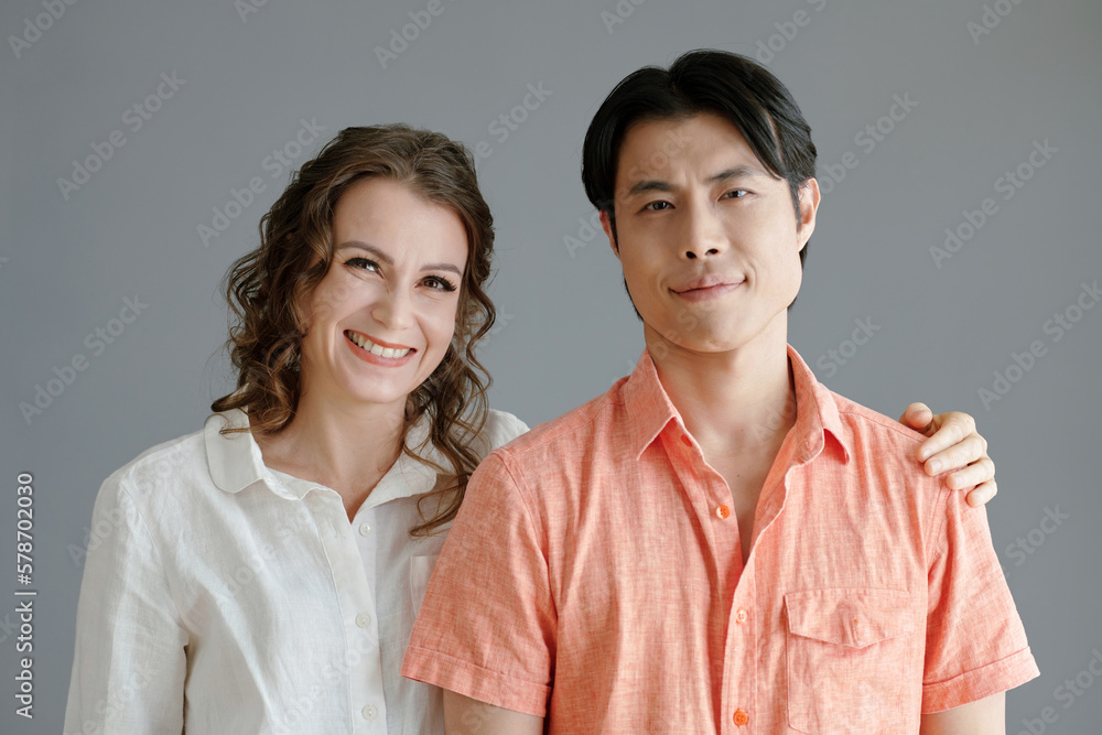 Portrait of smiling mature woman standing next to young Asian man and putting hand on his shoulder Portrait of smiling mature woman standing next to young Asian man and putting hand on his shoulder