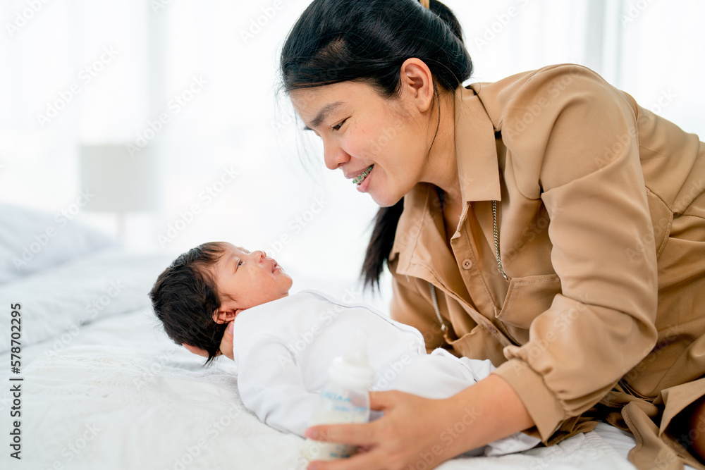 Asian mother hold newborn baby who look at her mother also stay on bed in bedroom of their house with day light. Asian mother hold newborn baby who look at her mother also stay on bed in bedroom of their house with day light.