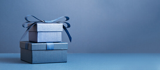 Two Luxury gift boxes with a blue bow on dark blue. Side view monochrome . Fathers day or Valentines day gift for him. Corporate gift concept or birthday party. Festive sale copy space banner