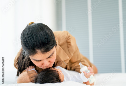 Close up Asian mother kiss her newborn baby who lie on bed with love and care in bedroom of their house.