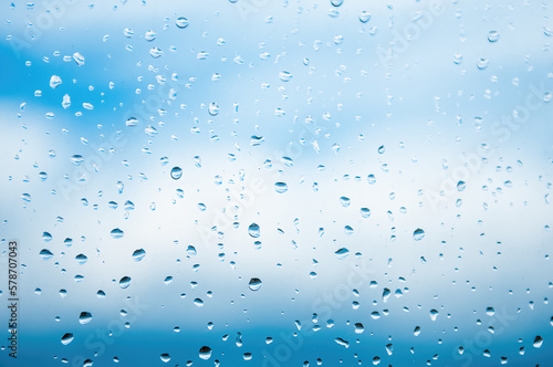 Raindrops on window glass against blue sky with white clouds. Place for text banner