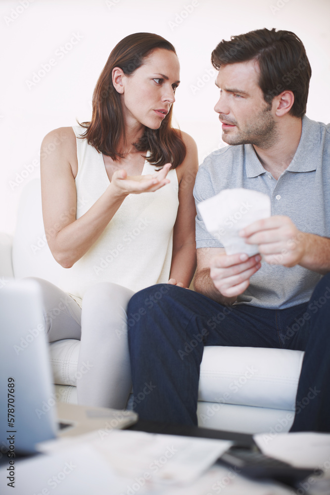 Sometimes there are disagreements on home finances. A married couple looking slightly concerned as they inspect bills and discuss their home finances.