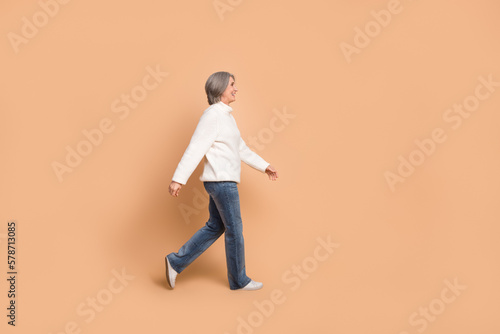 Full length photo of funky adorable lady dressed white sweater walking looking empty space isolated beige color background