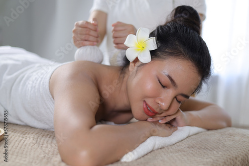 Woman Enjoying Herbal Massage. Relaxed Asian girl sleeping with eyes closed receiving traditional Thai herbal massage with fragrant bags. Body beauty treatment, relaxation and wellness.