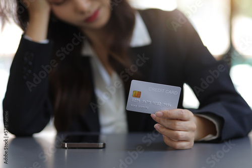 Woman holding credit card stressed out from debt and overburdened expenses.
