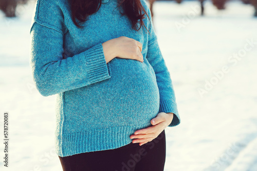 Pregnant woman's belly over winter background. Pregnant woman in blue sweater touching big belly with hands. photo